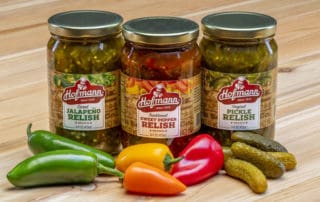 Hofmann Sweet Jalapeño Relish, Traditional Sweet Pepper Relish and Original Pickle Relish on table with ingredients