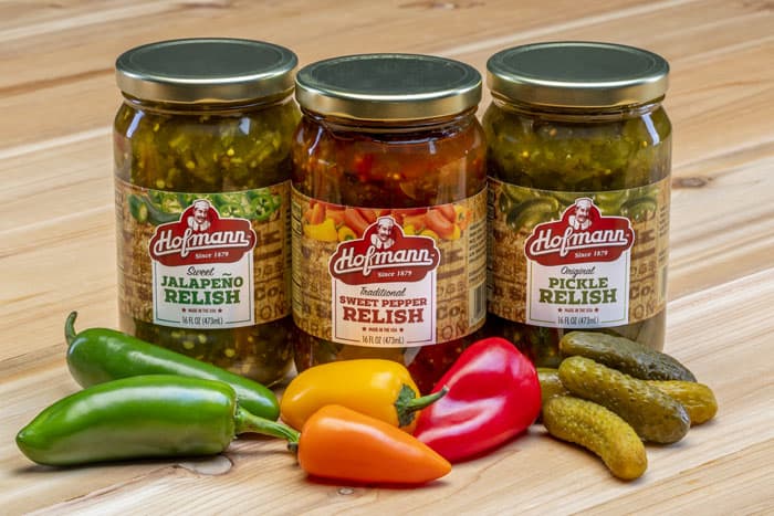 Hofmann Sweet Jalapeño Relish, Traditional Sweet Pepper Relish and Original Pickle Relish on table with ingredients